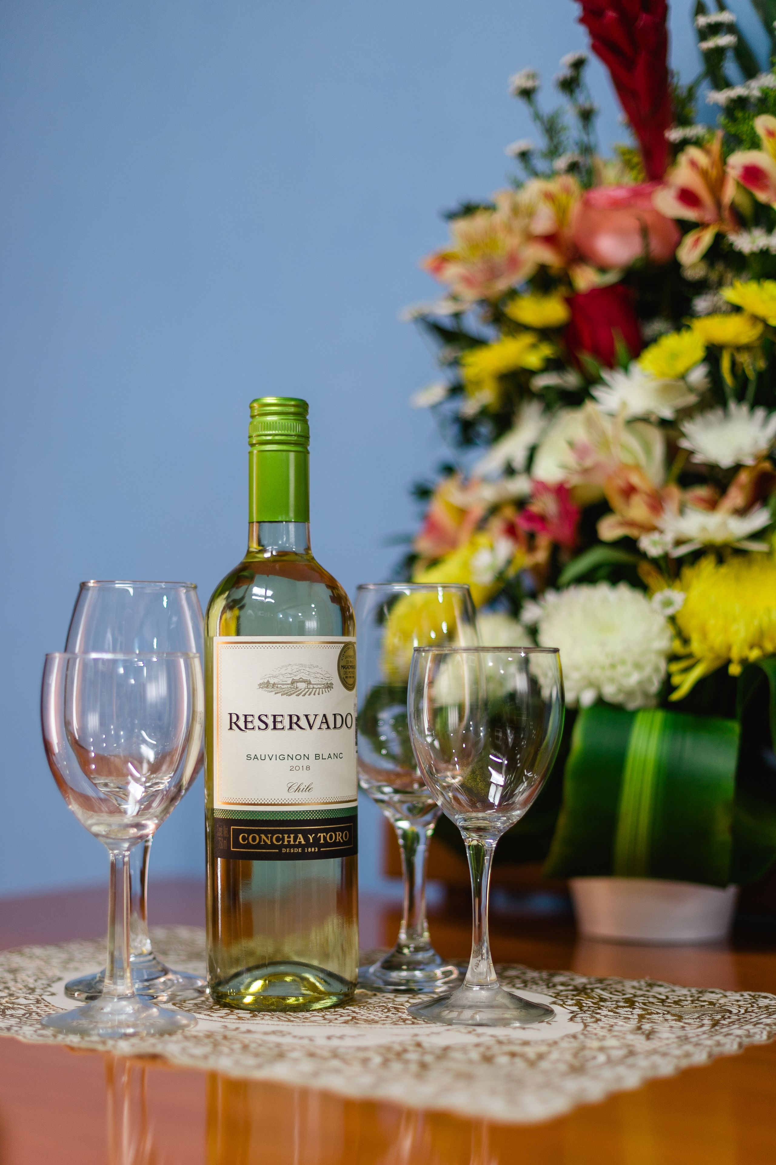 A bottle of Reserva Sauvignon Blanc 2018, two empty wine glasses, and a bouquet of flowers on a table.