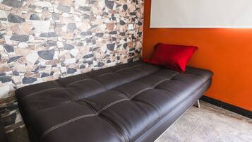 A dark brown leather sofa with a red cushion against a stone mosaic wall and an orange wall.