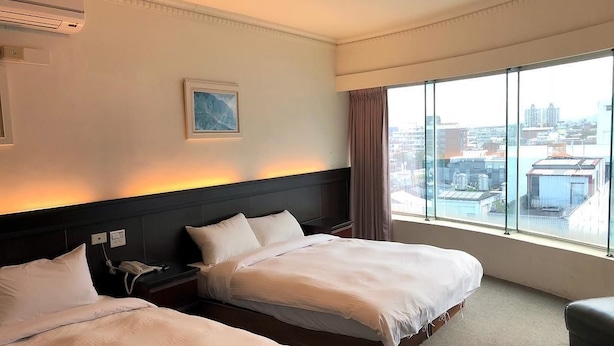 Habitación de hotel con dos camas, un ventanal con vistas a la ciudad, un cuadro en la pared y un equipo de aire acondicionado.