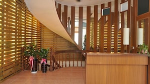 Un área de recepción con una escalera de madera curva, un ventilador de techo y plantas en macetas.