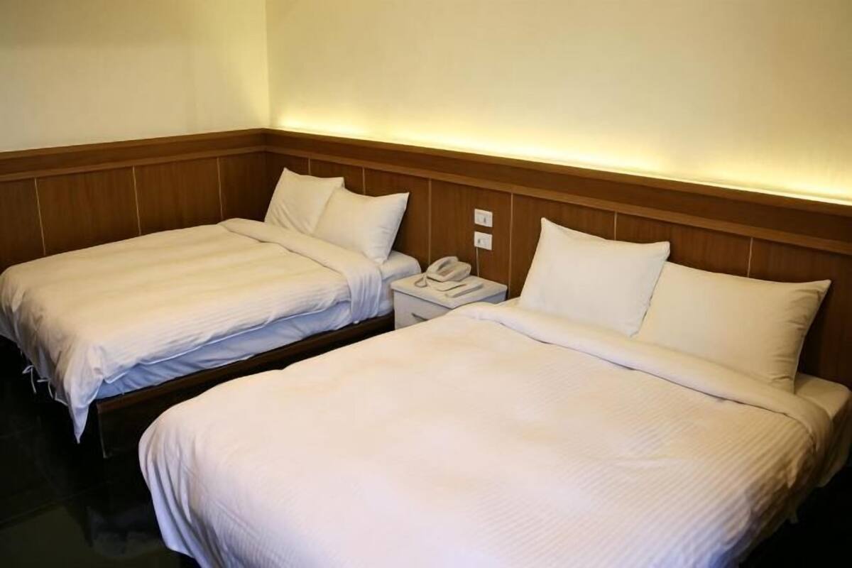Dos camas individuales con cabeceros de madera, una mesita de noche con teléfono y una lámpara de pared.