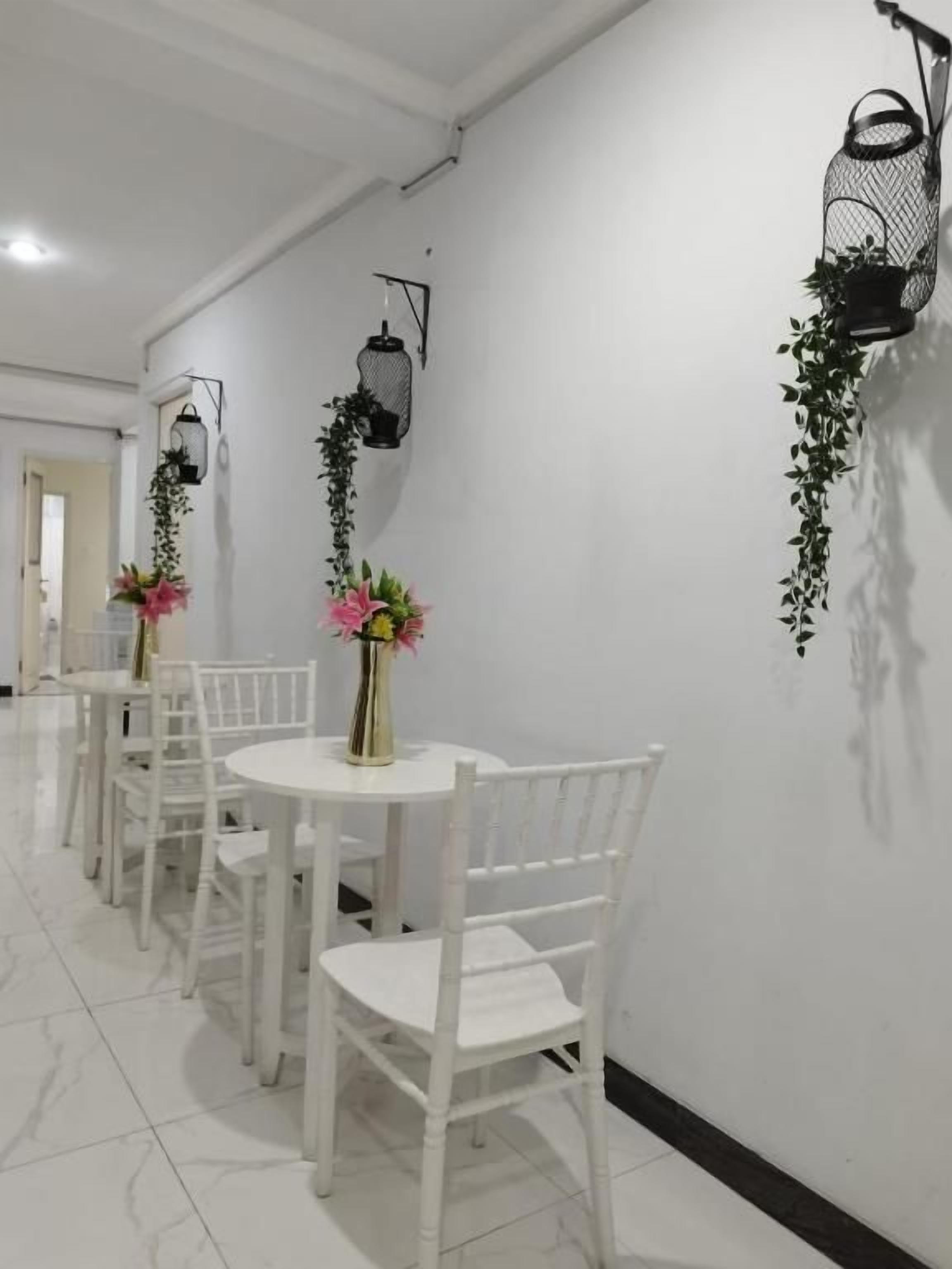 A corridor with white chairs and tables, black wall-mounted lanterns, and hanging plants.