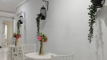 A corridor with white chairs and tables, black wall-mounted lanterns, and hanging plants.