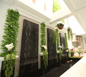 A modern interior with a black marble wall, green plants, and a water feature. - Nest Residence (Jakarta)