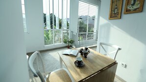 A dining area with a wooden table, white chairs, and a potted plant. - Nest Residence (Jakarta)