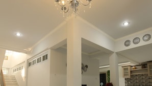 A spacious interior with a grand chandelier, a staircase, and a kitchen area. - Nest Residence (Jakarta)
