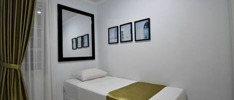 A single-bed room with a large mirror, three framed pictures, and a gold accent on the bed.