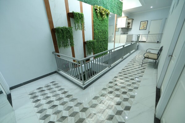 Un interior moderno con suelo de baldosas, un balcón con barandilla y una pared con plantas verticales.