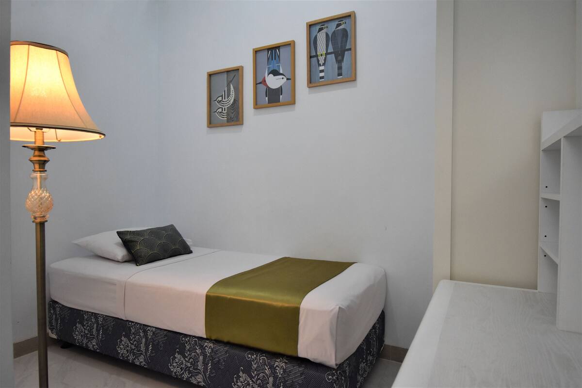 A neatly arranged bedroom with a bed, bedside lamp, and three framed artworks on the wall.