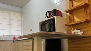 A compact kitchen with a microwave, a small refrigerator, and a wooden shelf above the counter. There are two woven stools and a wooden cabinet with a shelf. - Verde Vida Apart Hotel (Pucón)