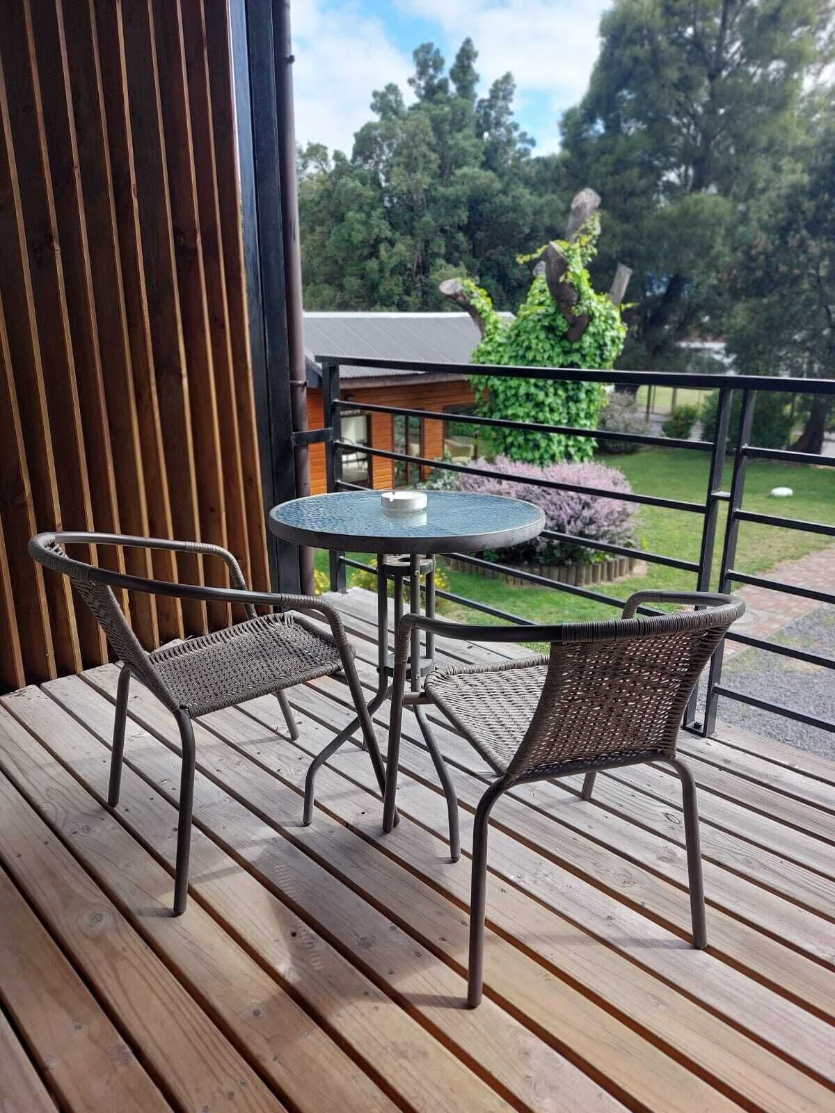Eine Holzterrasse mit zwei Korbstühlen und einem kleinen runden Tisch.
