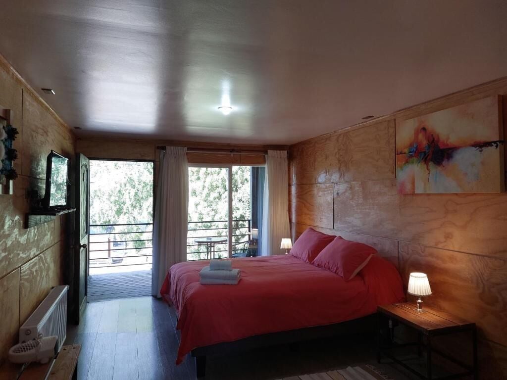 Une chambre à coucher avec un lit, une table de chevet avec une lampe, une fenêtre avec des rideaux et une vue sur l’extérieur.