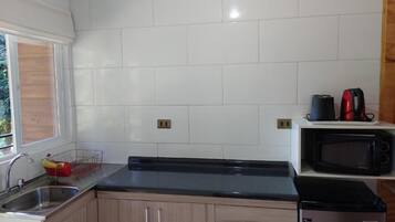 A kitchen with white tiles, a black countertop, a sink, a microwave, and a refrigerator.