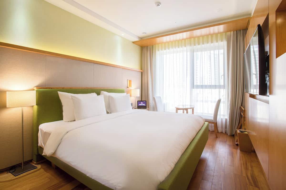 A hotel room with a large bed, a flat-screen TV, a desk with a chair, and a window with curtains.