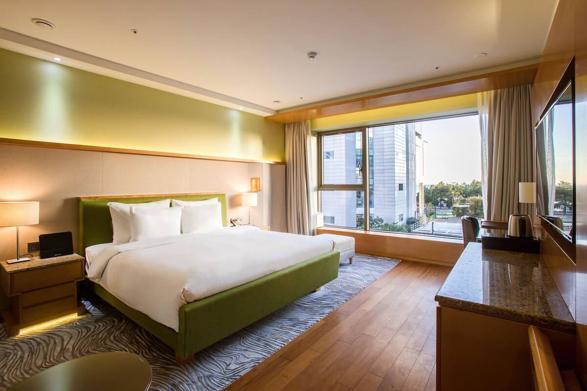 A hotel room with a large bed, a desk, a chair, and a view of the city.