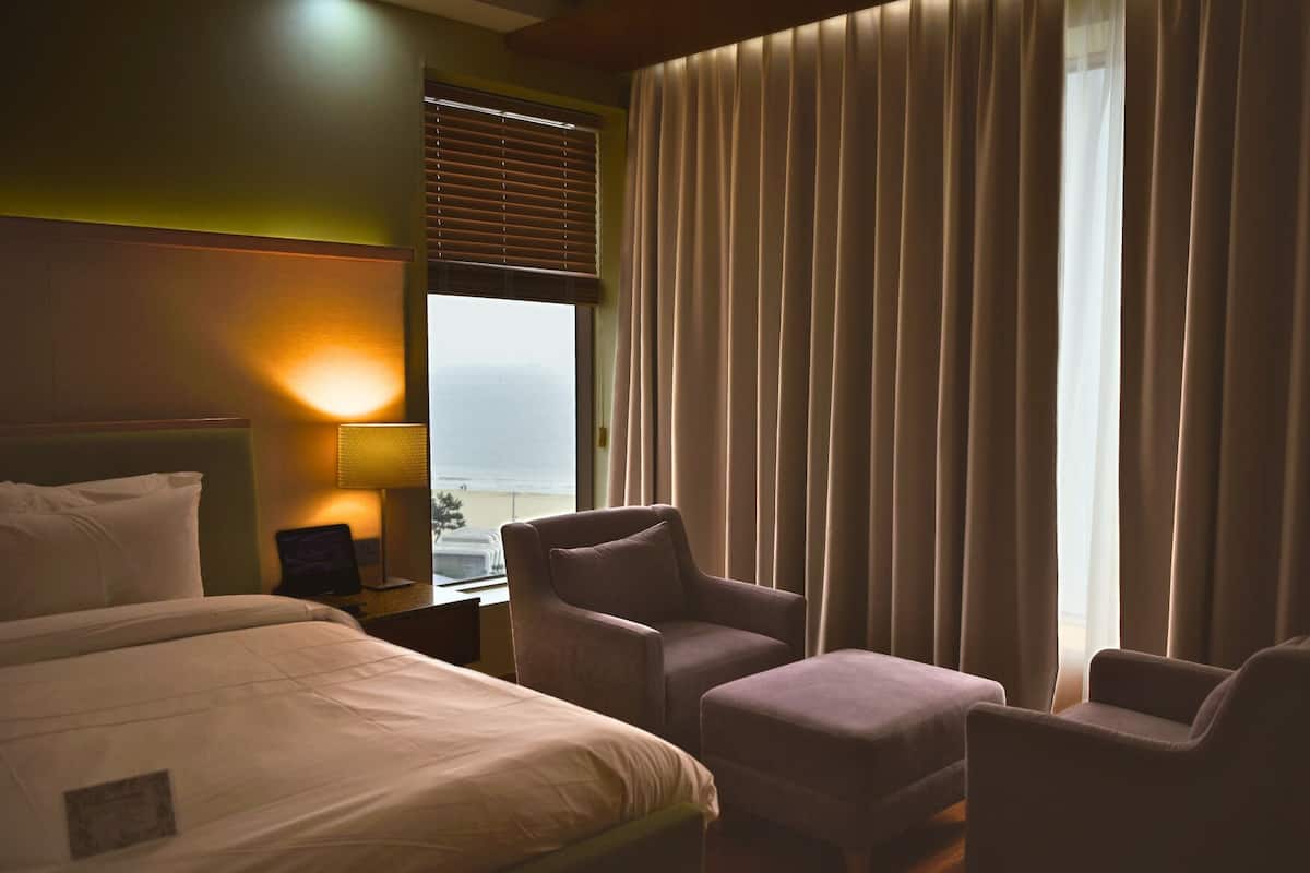 A hotel room with a bed, two armchairs, a nightstand, a lamp, and a window with curtains.