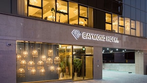 The exterior of the Baymond Hotel with a modern facade, large glass windows, and a prominent hotel sign.