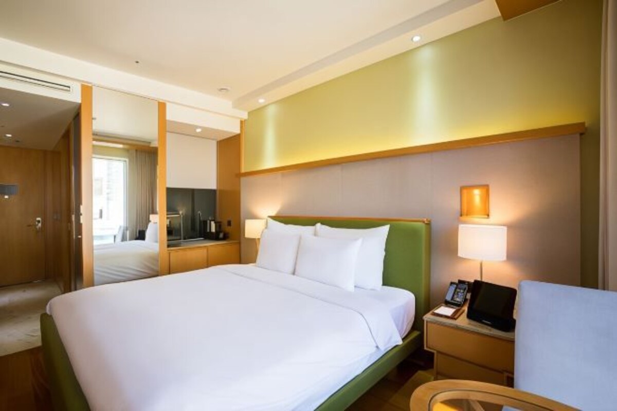A hotel room with a large bed, a bedside table with a lamp, a chair, and a mirror.