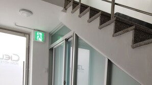 Un hall de hotel con un ascensor de vidrio, un letrero de salida de emergencia visible y un suelo pulido.