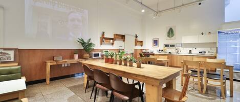 Een moderne keuken met houten kastjes, een groot eiland en een scherm waarop iemand wordt geprojecteerd.