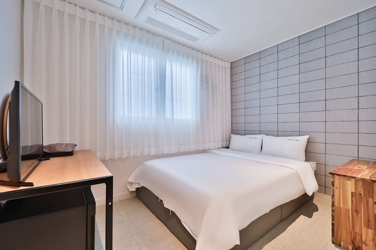 Une chambre d’hôtel moderne avec un grand lit, un bureau équipé d’un ordinateur et une fenêtre agrémentée de rideaux légers.