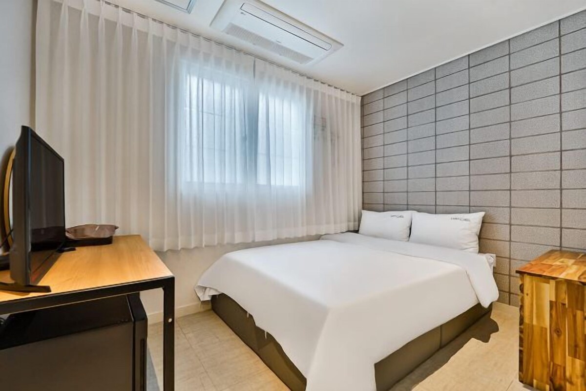 Ein Hotelzimmer mit einem Bett, einem Schreibtisch mit Computer, einem Fernseher und einem Fenster mit Vorhängen.