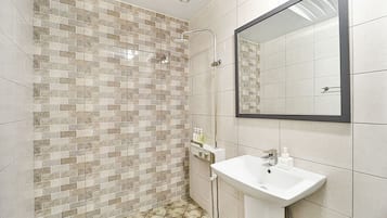 A bathroom with a tiled shower wall, a sink, and a mirror.