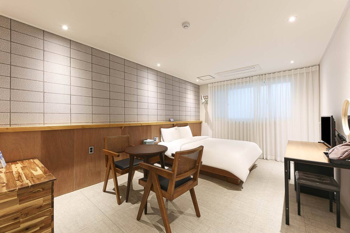 Une chambre d’hôtel équipée d’un lit, d’un bureau, d’une chaise, d’une petite table et d’un téléviseur fixé au mur.
