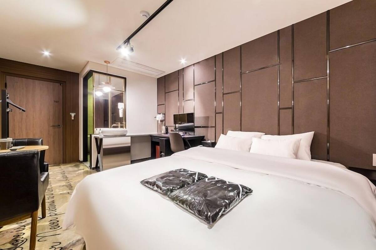 A modern hotel room with a large bed, a desk, a chair, and a mirror.
