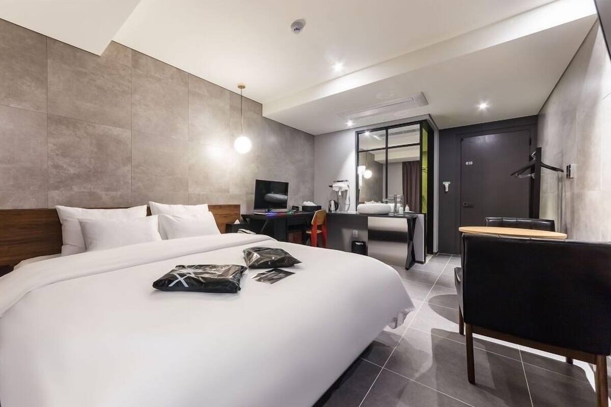 A modern hotel room with a large bed, a desk, a chair, and a bathroom.