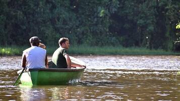 A small green boat with two people rowing on a calm river surrounded by greenery.