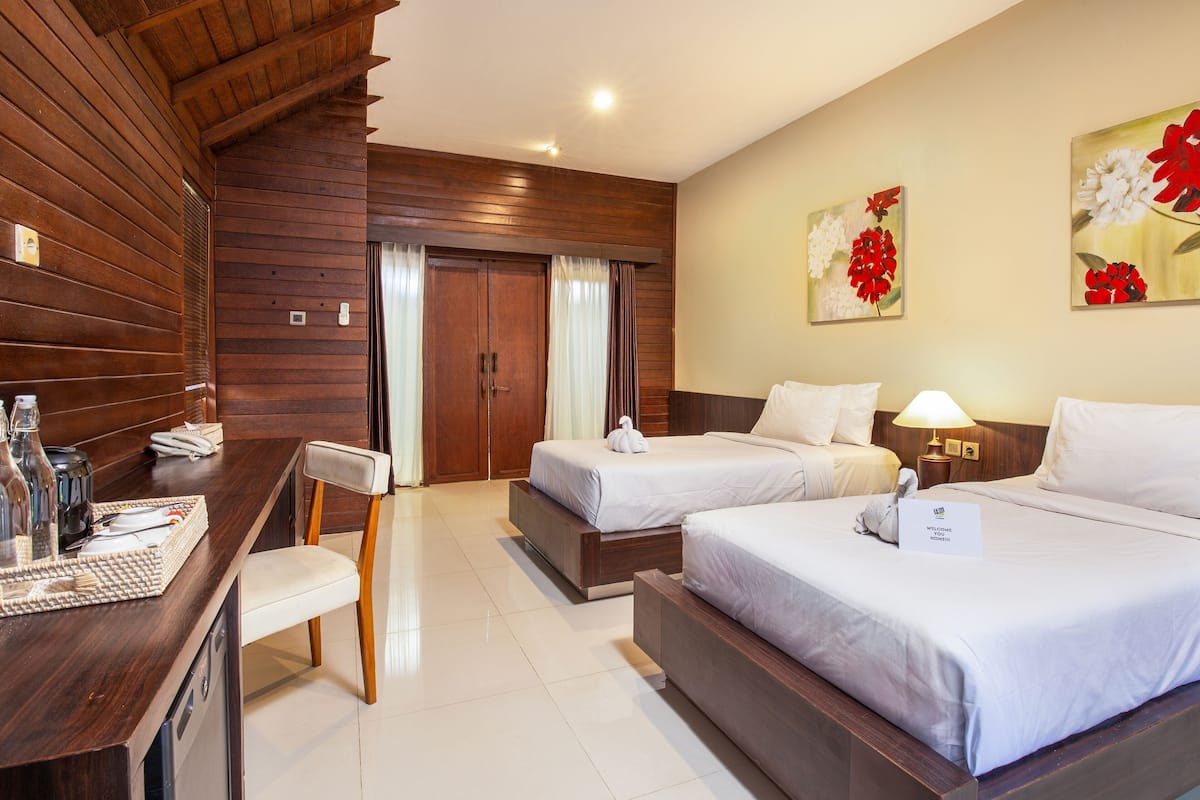 A hotel room with two beds, a desk with a chair, a minibar, and a bathroom with a wooden door.