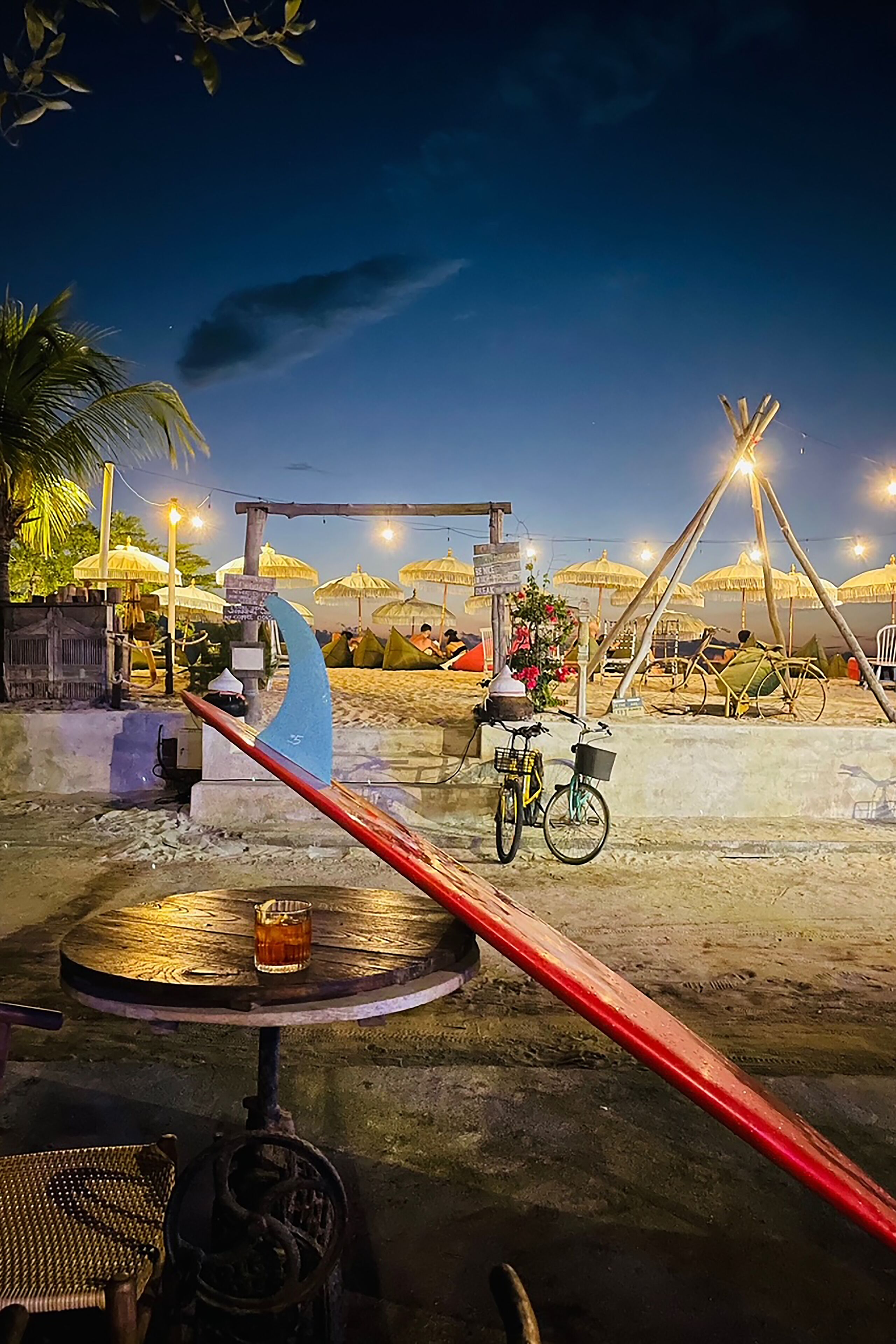 A beachside restaurant with outdoor seating, a bicycle, and a unique blue water feature.