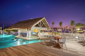 Un área de piscina con una estructura de techo de paja, un bar y asientos al aire libre.