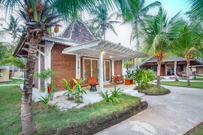 Ein Bungalow mit Ziegelaußenwand, einer Veranda mit Gartenmöbeln und einer Palme im Vordergrund.