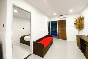 Habitación de hotel moderna con un sofá de color rojo, un espejo grande y vista a un área de piscina al aire libre.