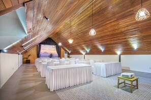 Une pièce spacieuse avec un plafond en pente, plusieurs tables recouvertes de nappes blanches et des lampes suspendues.