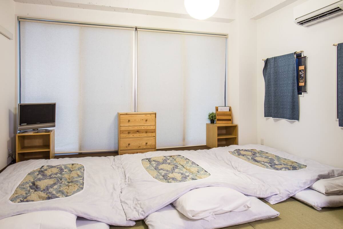 Une chambre avec deux lits, une télévision, une commode et une porte coulissante.
