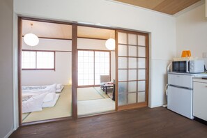 Een traditionele Japanse kamer met tatami vloerbedekking, een futon bed, schuifdeuren van shoji papier, een klein tafeltje en een magnetron.