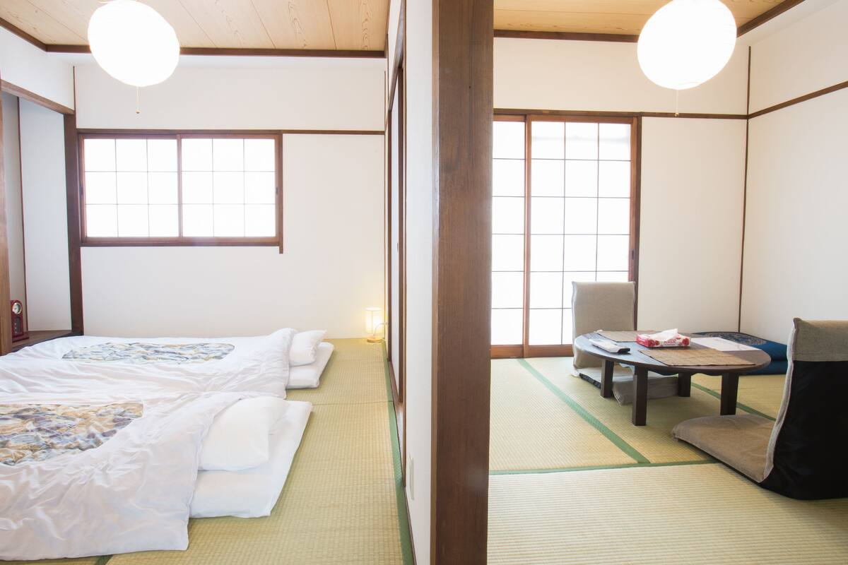 Une pièce de style japonais traditionnel, avec un sol recouvert de tatamis, un futon servant de lit, une petite table basse et une chaise.