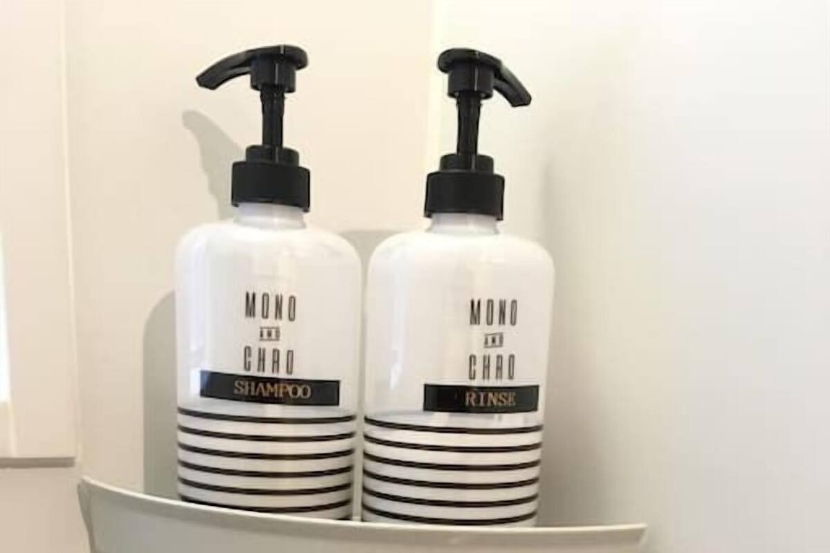 Une étagère de salle de bain avec deux flacons blancs étiquetés « MONO CHARO SHAMPOO » et « MONO CHARO RINSE », et un flacon transparent à rayures noires.