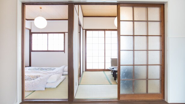 Een traditionele Japanse kamer met tatami vloerbedekking, een futonbed, schuifdeuren van shoji-papier en een hanglamp.