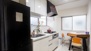 Een moderne keuken met een zwarte koelkast, witte kasten, een raam en een eethoek met een houten tafel en twee stoelen.
