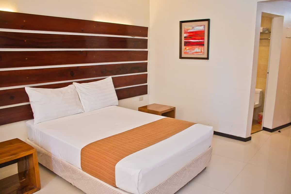 A neatly made bed with a wooden headboard, a white pillow, and a brown throw blanket. There is a small wooden nightstand beside the bed, and a framed picture on the wall.