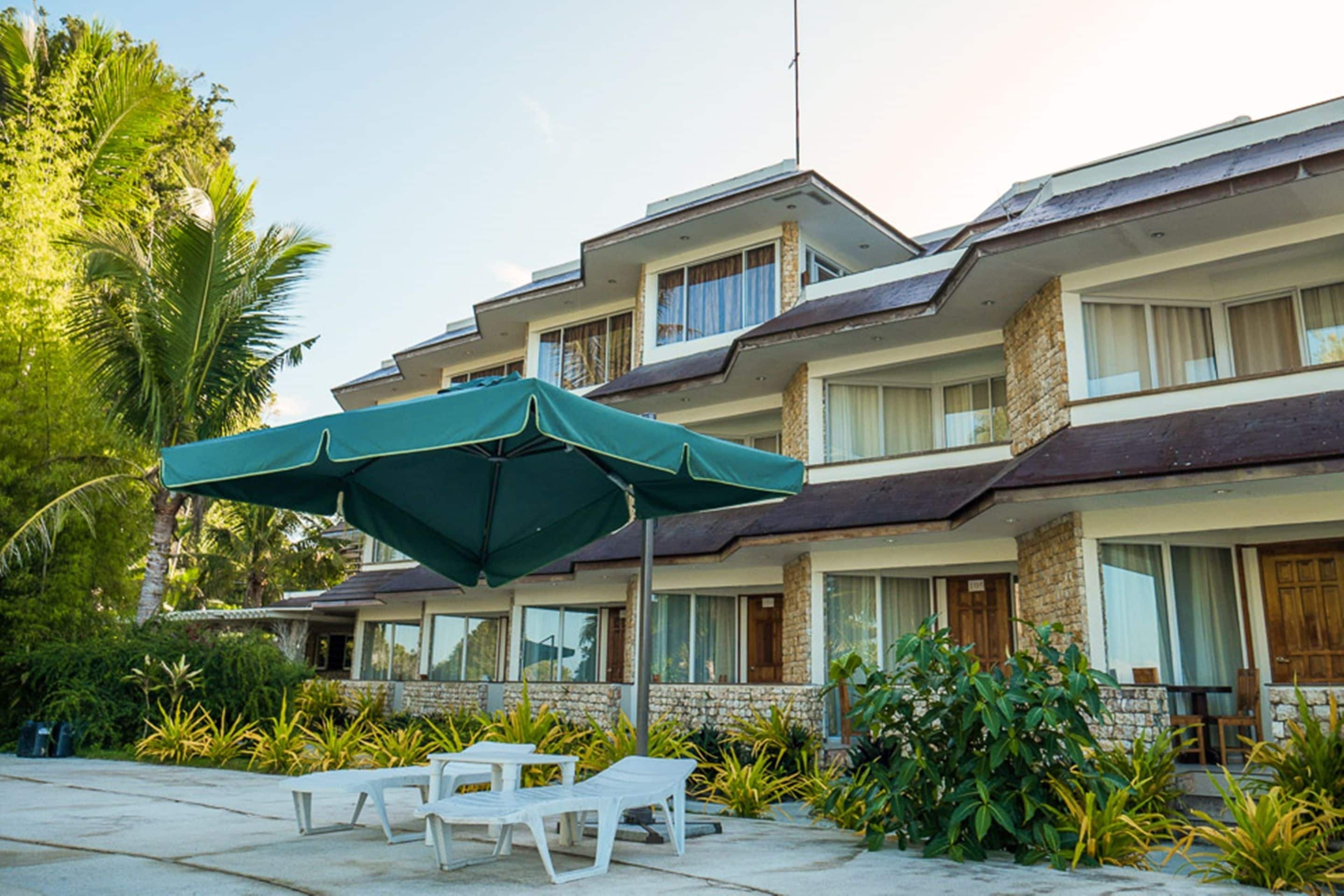 Un hotel de varios pisos con balcón, zona de estar al aire libre y abundante vegetación.