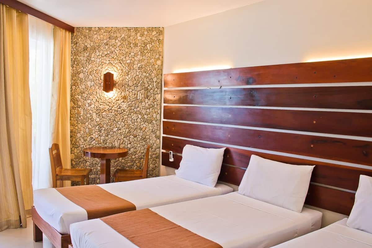 A hotel room with two beds, a stone wall, a wooden headboard, a round table, and a chair.