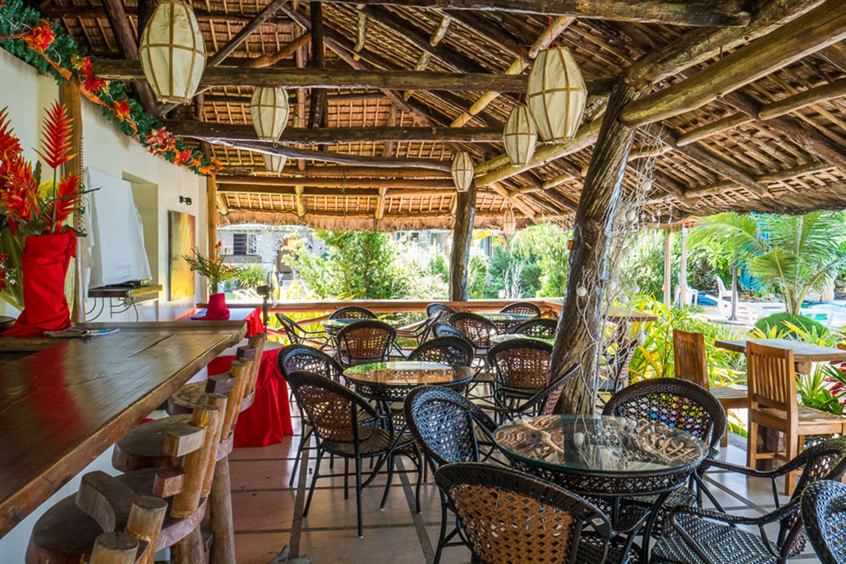 An outdoor dining area with thatched roof, wicker furniture, and potted plants.