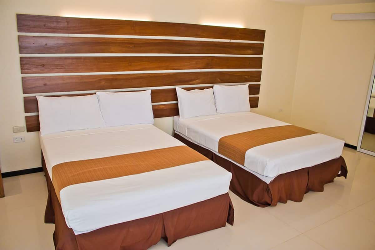 A hotel room with two beds, each with white linens and brown bed skirts. The headboard is wooden with horizontal planks.