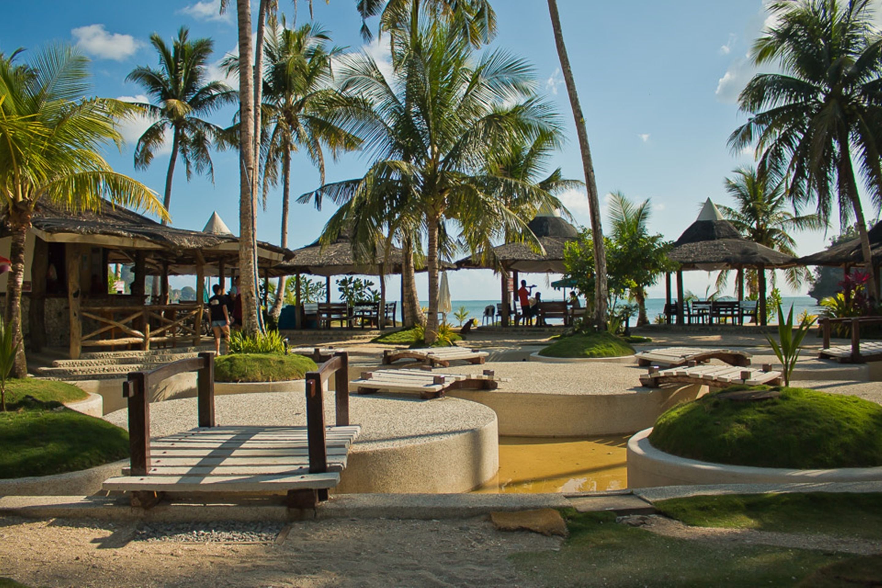 A resort with palm trees, thatched-roof structures, and a beach view.
