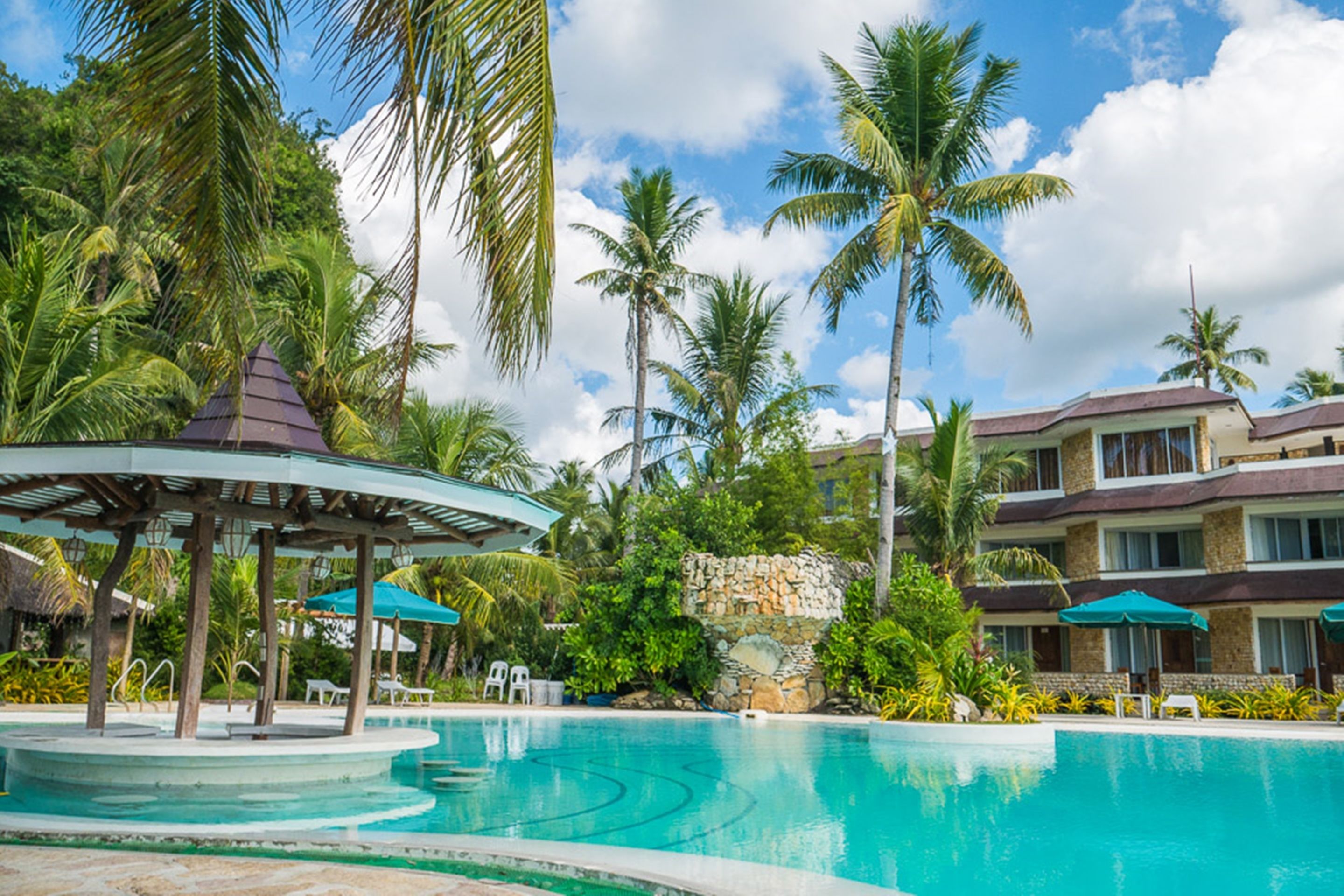 A resort pool area with a gazebo, palm trees, and a stone wall.
